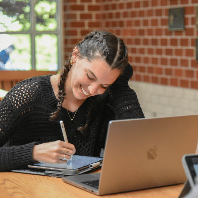 HRA student working on her homework at a table with laptop and tablet, representing HRA's new website