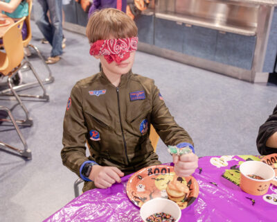 HRA Middle Schooler decorating a cupcake blindfolded at Halloween Happenings 2025