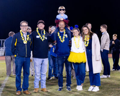 HRA varsity swimming coach Jeff Scott with alumni and former swimmers Mitchell Finch '08, Chase Suttle '17, Caroline Thatcher '16, and Peyton Baldwin '15, as well as his son Patrick, on the football field at Homecoming 2025