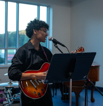 HRA senior Aaron Carlson '27 singing and playing the guitar in the Mary and Larry Pope Dining Hall