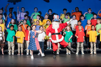 HRA Lower School students performing on stage with Santa Claus in a patriotic hat