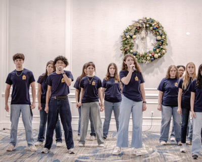 HRA students Aaron Carlson '27 and Heather Lowekamp '26 performing with the a cappella group Nowhere to Hide with a holiday wreath in the background