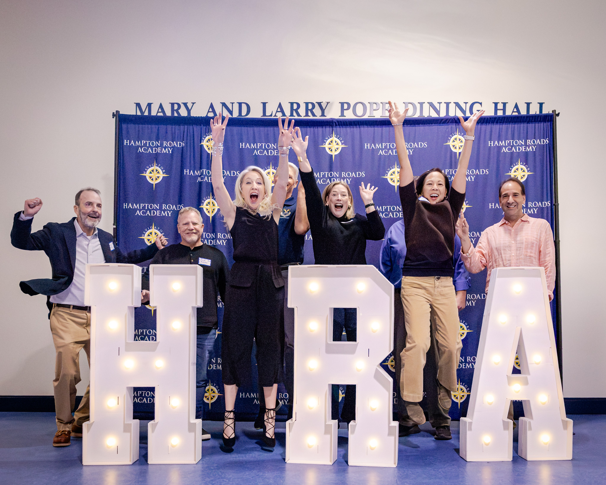 Members of the HRA Class of 1986 excitedly jumping during a photo with large illuminated letters "H-R-A"
