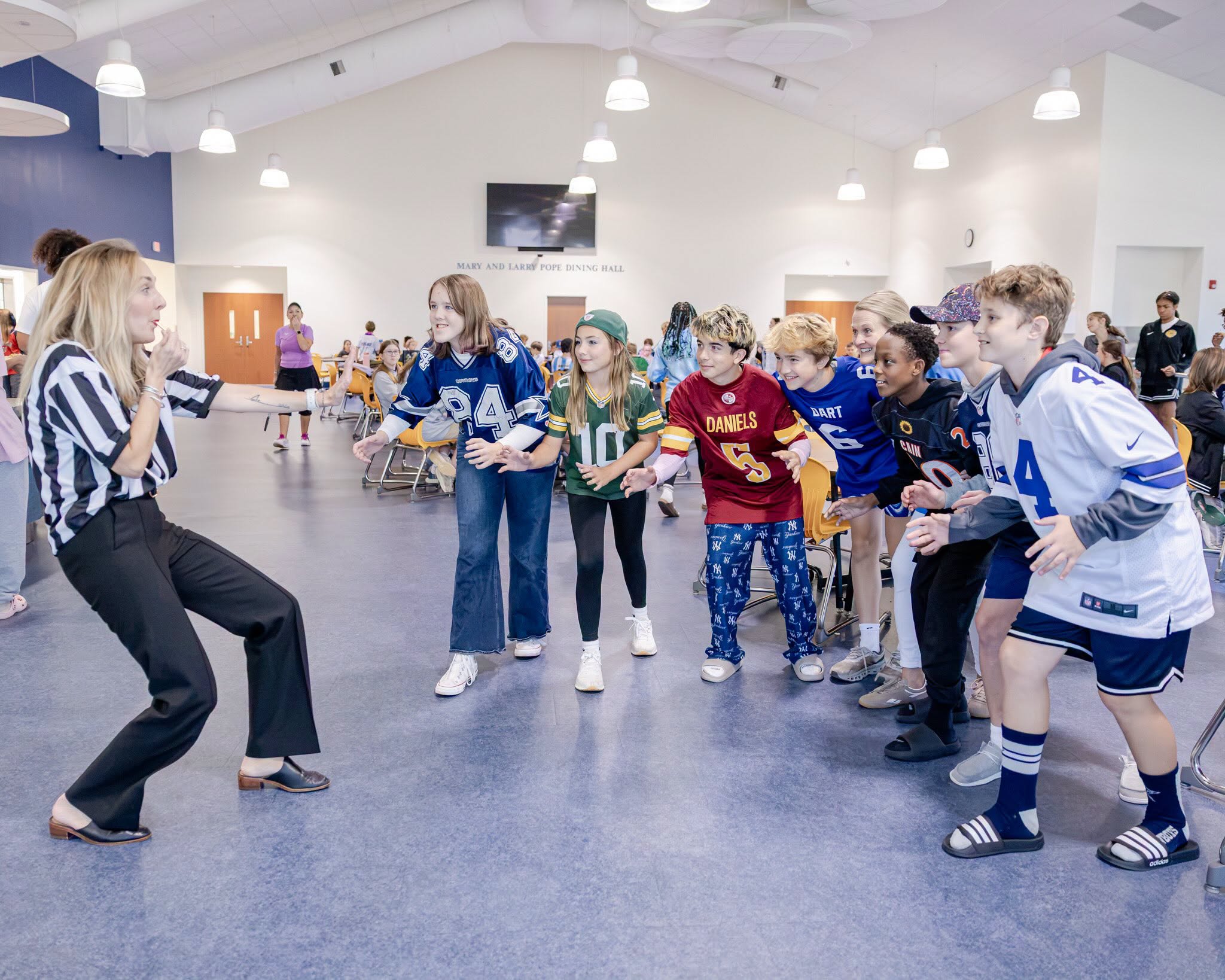 HRA Director of Middle School Abigail Whorley, dressed as a referee and blowing a whistle, with a group of Middle School students in sports jerseys